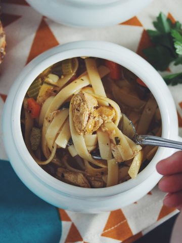 overhead of a bowl of vegan chicken noodle soup with a spoon lifting some out