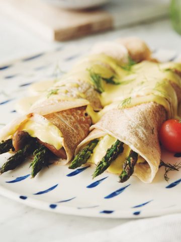 side angle of two vegan crepes with asaparagus mushroom and hollandaise sauce on a plate