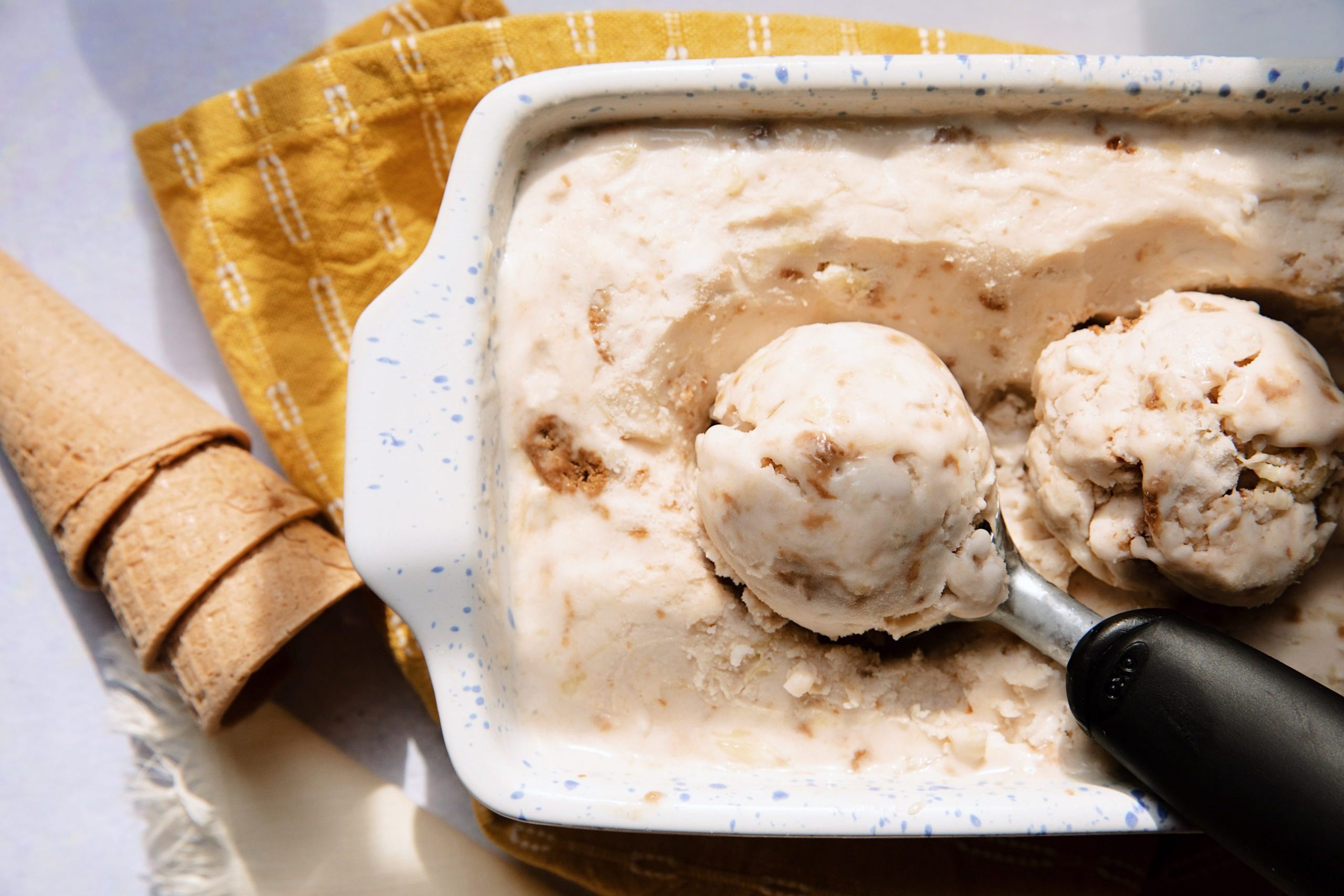 overhead of pineapple ginger snap ice cream in a baking dish with a ice cream scoop and cones